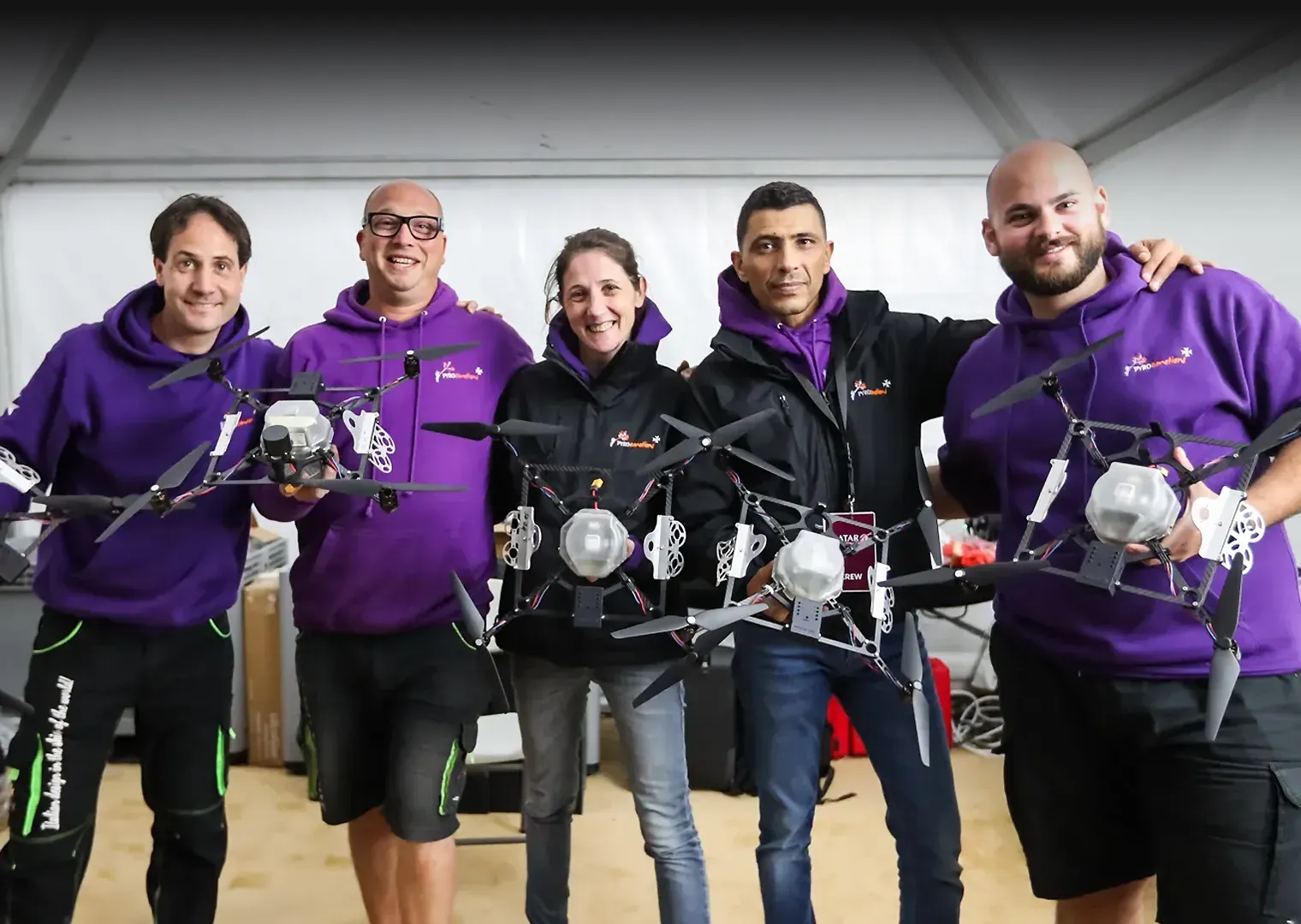 Team holding pyrotechnic drones and smiling in a setup tent